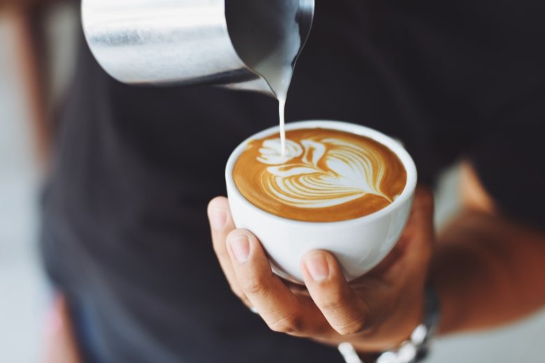 Ein Mann gießt mit Latte Art das Muster einer Tulpe in eine Kaffeetasse